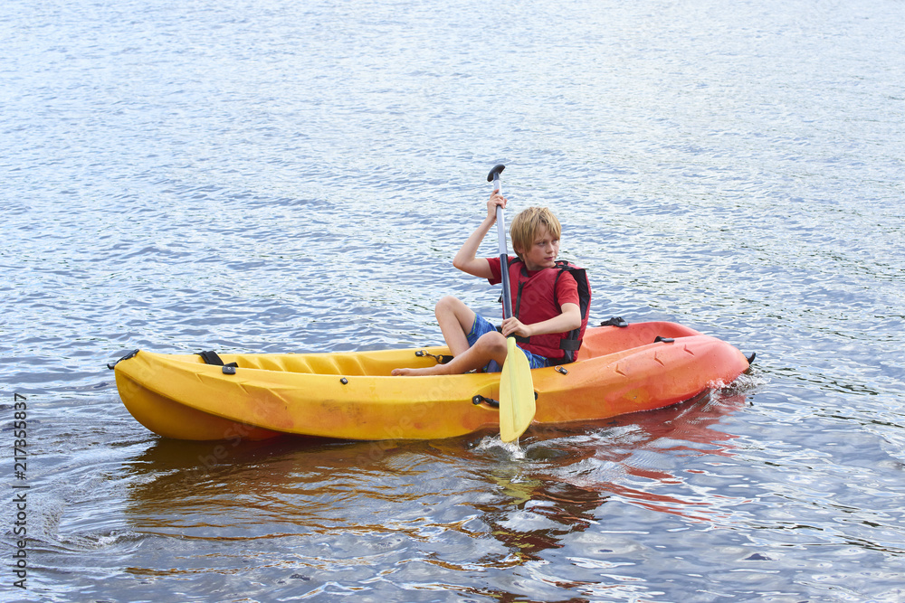 Active happy child. Teenage school boy having fun enjoying adventurous experience kayaking on the lake on a sunny day during summer vacation