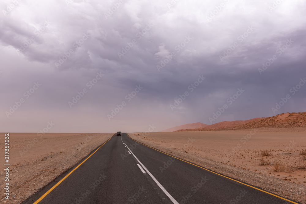 Single car on asphalt road in desert sand region with stormy overcast sky