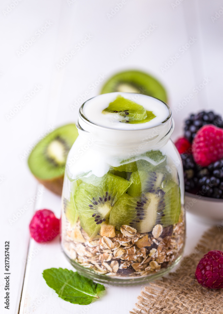 White yogurt with muesli in glass bowl with pieces of kiwi on top. White yogurt with muesli in glass bowl with pieces of kiwi on top.