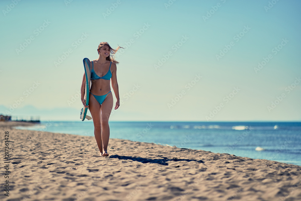 Smiling surfer girl walking with board on the sandy beach. Healthy Active Lifestyle. Surfing. Summer Vacation. Extreme Sport.. Smiling surfer girl walking with board on the sandy beach. Healthy Active Lifestyle. Surfing. Summer Vacation. Extreme Sport..