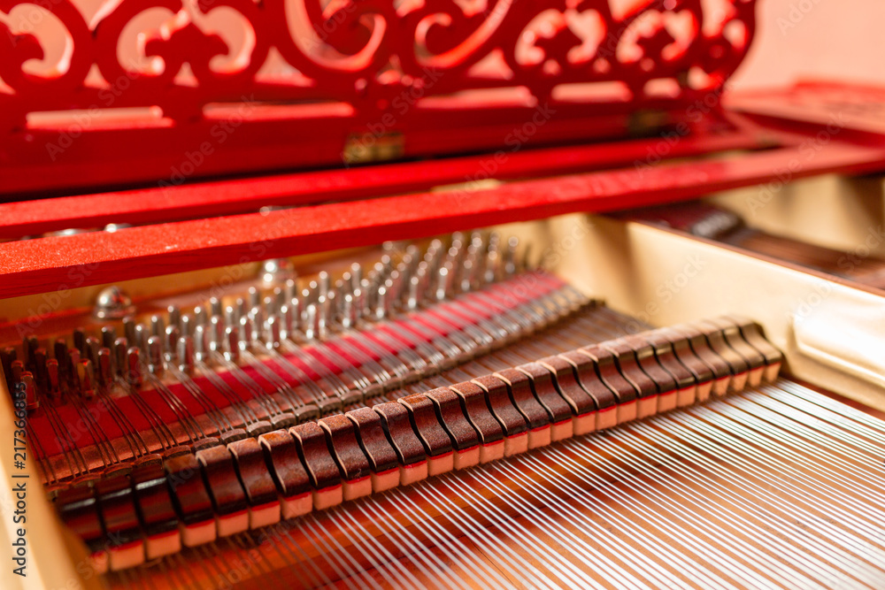 Strings inside a red grand piano. Piano playing, dampers, felt hammers, bronze strings and metal frame.