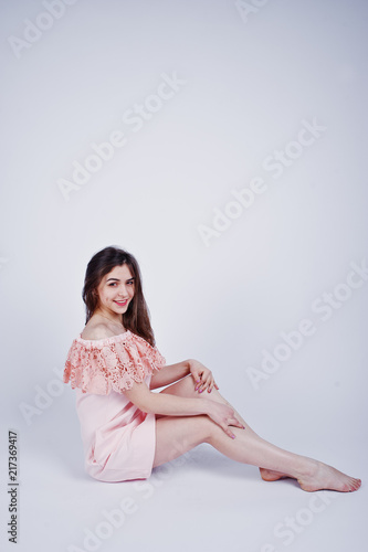 Portrait of a fashionable woman in pink dress sitting and posing on the floor in the studio.