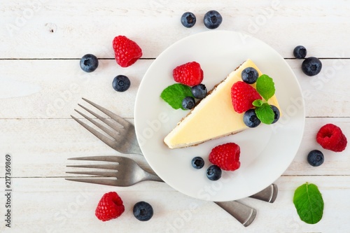 Slice of cheesecake with blueberries and raspberries, top view scene over a bright, white wood background