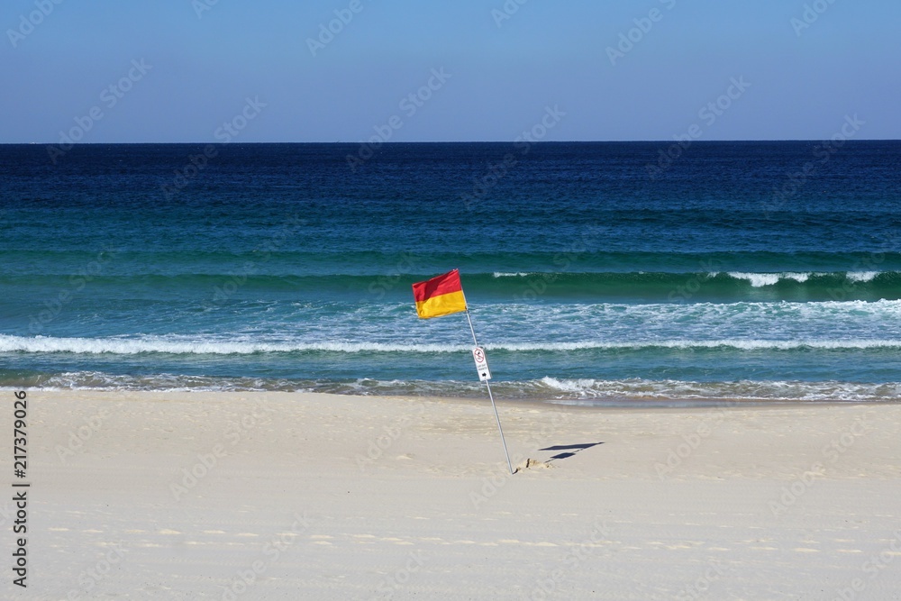 Red and Yellow Surf Life Saving Flag on White Sand against Blue Sky Red and Yellow Surf Life Saving Flag on White Sand against Blue Sky