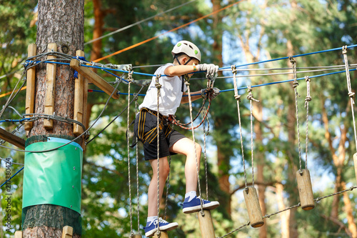 cute boy in white t shirt in the adventure activity park with helmet and safety equipment. Young boy playing and having fun doing activities outdoors. Hobby, active lifestyle concept