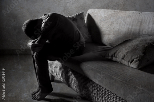 lifestyle dramatic light portrait of young sad and depressed man sitting at shady home couch in pain and depression feeling stressed and desperate © TheVisualsYouNeed