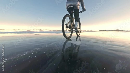 Woman is riding bicycle on the ice. The girl is dressed in a silvery down jacket, cycling backpack and helmet. Ice of the frozen Lake Baikal. The tires on the bicycle are covered with special spikes photo