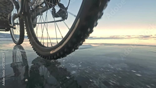 View of the tire. Shooting 60fps actioncam. Woman is riding bicycle on the ice. Ice of the frozen Lake Baikal. The tires on the bicycle are covered with special spikes. The traveler is ride a cycle. photo