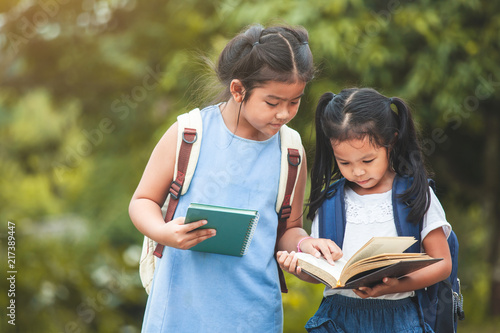 Back to school. Cute asian child girl with school bag reading a book with her sister together in nature background