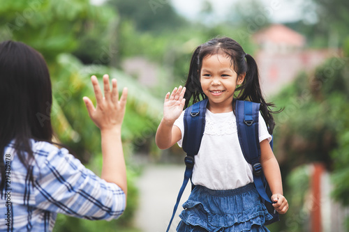 Back to school. Cute asian child girl with school bag and her mother making hi five gesture before go to school with fun