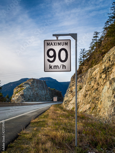 Speed limit sign with a keep right sign in the background beside a mountain highway.