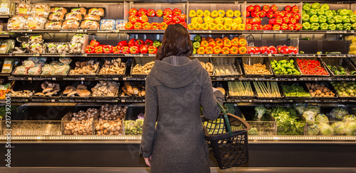 Φωτογραφία Woman standing in front of a row of produce in a grocery store.