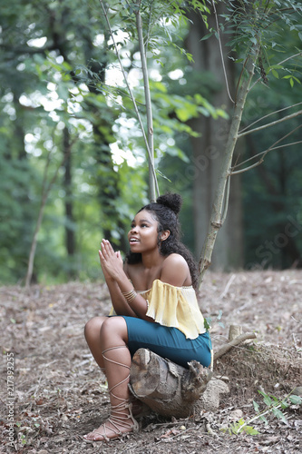 Beautiful black woman sitting in woods and praying