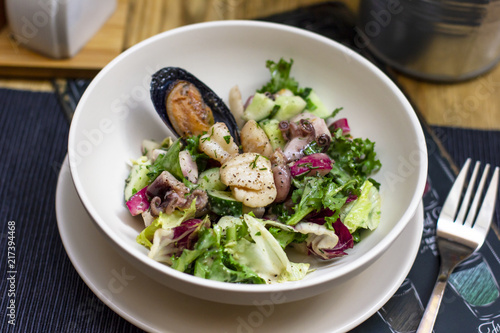 Warm salad with seafood mussels  octopus and fresh vegetables in deep plate on the table