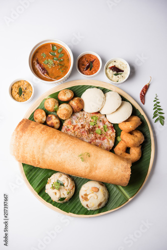 Group of South Indian food like Masala Dosa, Uttapam, Idli/idly, Wada/vada, sambar, appam, semolina halwa, upma served over banana leaf with colourful chutneys, selective focus