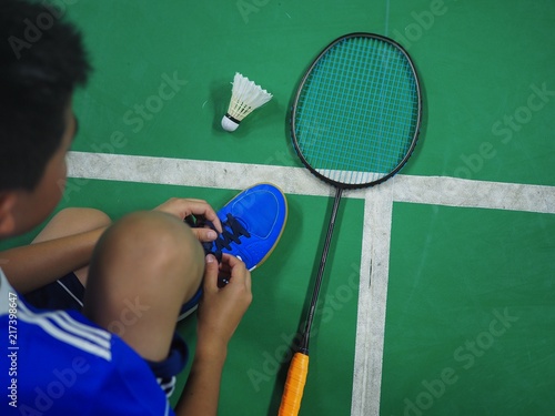 Asian boy tie shoe laces inside badminton court.