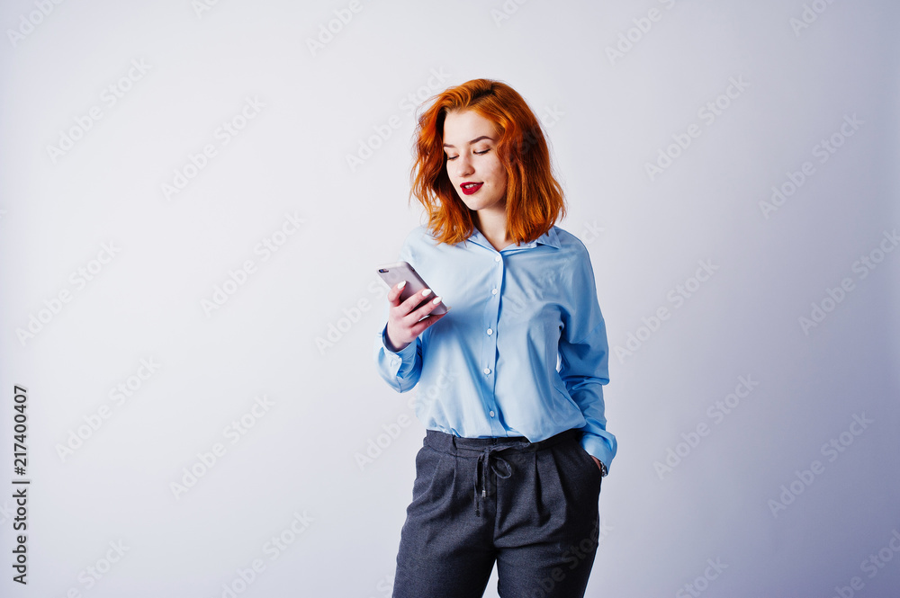 Portrait of a young redheaded businesswoman in blue shirt and trousers texting on the phone. Portrait of a young redheaded businesswoman in blue shirt and trousers texting on the phone.