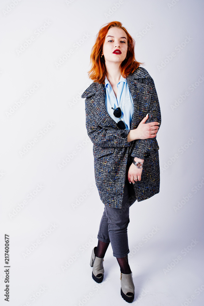 Portrait of a fantastic redheaded girl in blue shirt, grey overcoat posing with sunglasses in the studio. Portrait of a fantastic redheaded girl in blue shirt, grey overcoat posing with sunglasses in the studio.