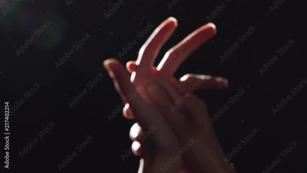 Silhouette portrait of two caucasian female arms closeup rubbing hands in light with flying dust into air, isolated over black background Silhouette portrait of two caucasian female arms closeup rubbing hands in light with flying dust into air, isolated over black background