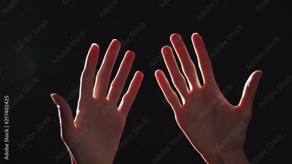 Silhouette portrait of two caucasian female arms closeup raised upward and turning against shining or lighting, isolated over black background Silhouette portrait of two caucasian female arms closeup raised upward and turning against shining or lighting, isolated over black background