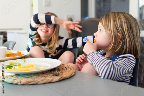 Two sisters sitting at the dinner table eating dinner and playing