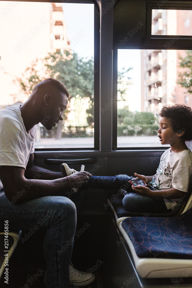 Side view of father tying son's shoelaces while sitting in bus Side view of father tying son's shoelaces while sitting in bus