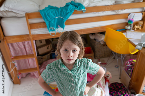 Female child standing in her messy bedroom with her school uniform on