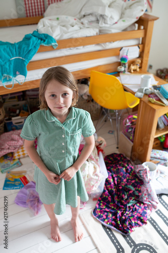 Female child standing in her messy bedroom with her school uniform on