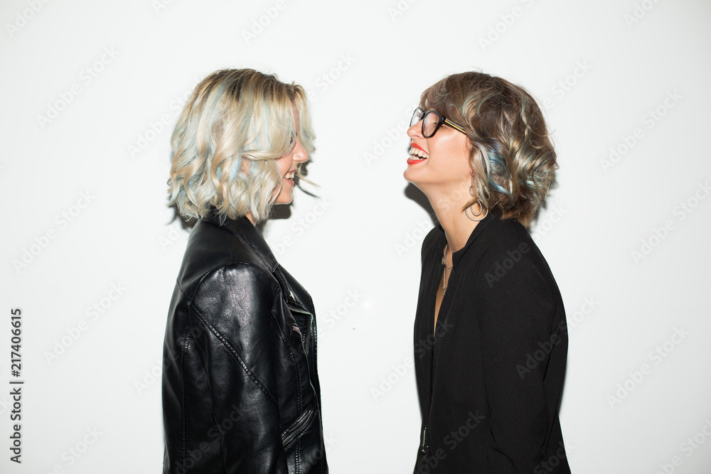 Pretty laughing girls in black jackets happily looking at each other over white background isolated Pretty laughing girls in black jackets happily looking at each other over white background isolated