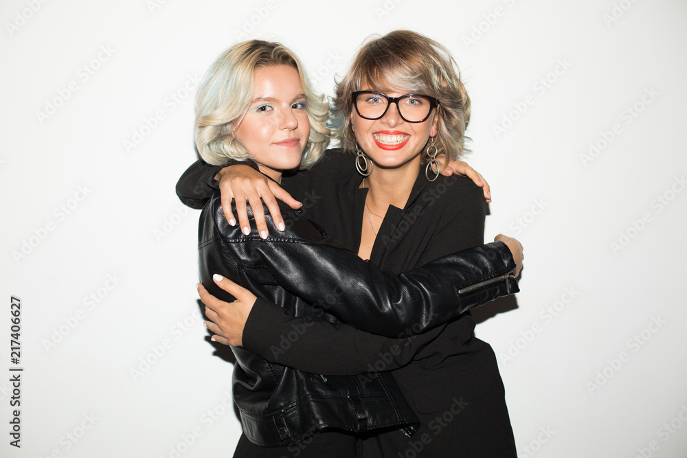 Pretty joyful girls in black jackets happily looking in camera hugging ...