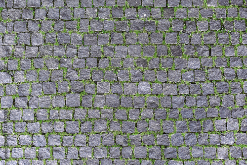 Overhead view of cobblestone street texture with grass . Stone pavement texture