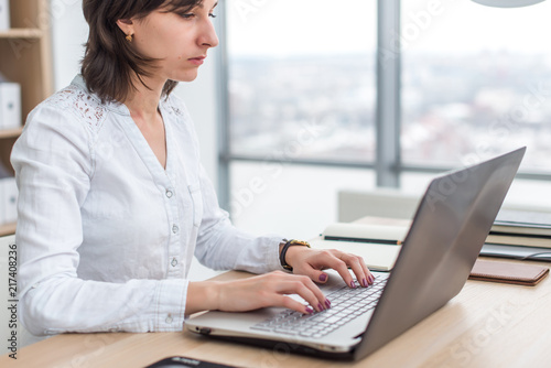 Office worker typing, working at her workplace, using laptop.