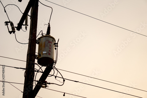 Old and vintage electric transformer on electricity post with electricity wires and other components in rural area of Thailand. Morning with soft light.