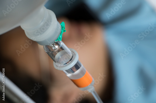 Close up saline solution drip with a patient lying on a bed on the background.