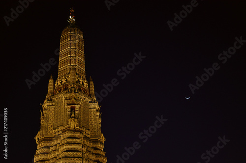 Low angle view of beautiful golden pagoda at night with moon, Wat Arun Ratchawararam, Bangkok Thailand.