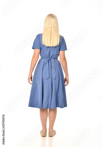 full length portrait of blonde girl wearing blue dress. standing pose with back to the camera. isolated on white studio background.