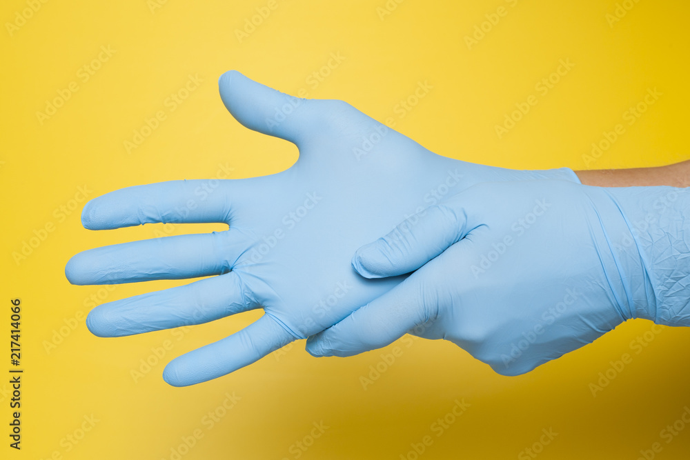 Doctor putting on protective blue gloves isolated on yellow background Doctor putting on protective blue gloves isolated on yellow background