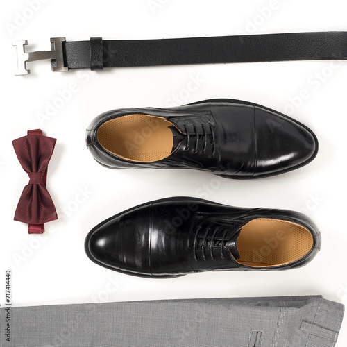 Close up of modern man accessories. Bordeaux bow tie, leather shoes, belt on white background. Set for formal style of wearing isolated on white background. Top view.