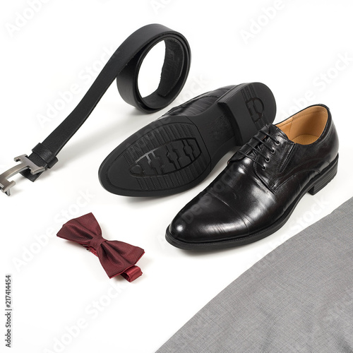 Close up of modern man accessories. Bordeaux bow tie, leather shoes, belt on white background. Set for formal style of wearing isolated on white background..