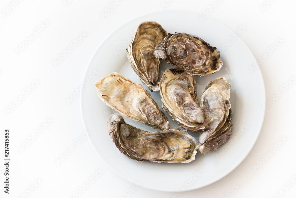 Fresh oysters. Raw fresh oysters on white round plate, image isolated, with soft focus. Restaurant delicacy. Saltwater oysters. Fresh oysters. Raw fresh oysters on white round plate, image isolated, with soft focus. Restaurant delicacy. Saltwater oysters.