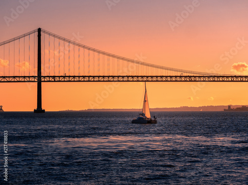Sailing boat in front of the bridge in Lisbon during sunset. clear sky. sunset scene