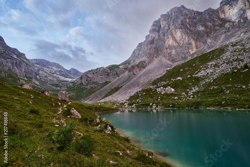 Partnunsee, türkisblauer Bergsee und Gebirgslandschaft im Abendlicht, blauer Himmel mit Wolken, schroffe Felsen, Alpwiese mit Wanderweg