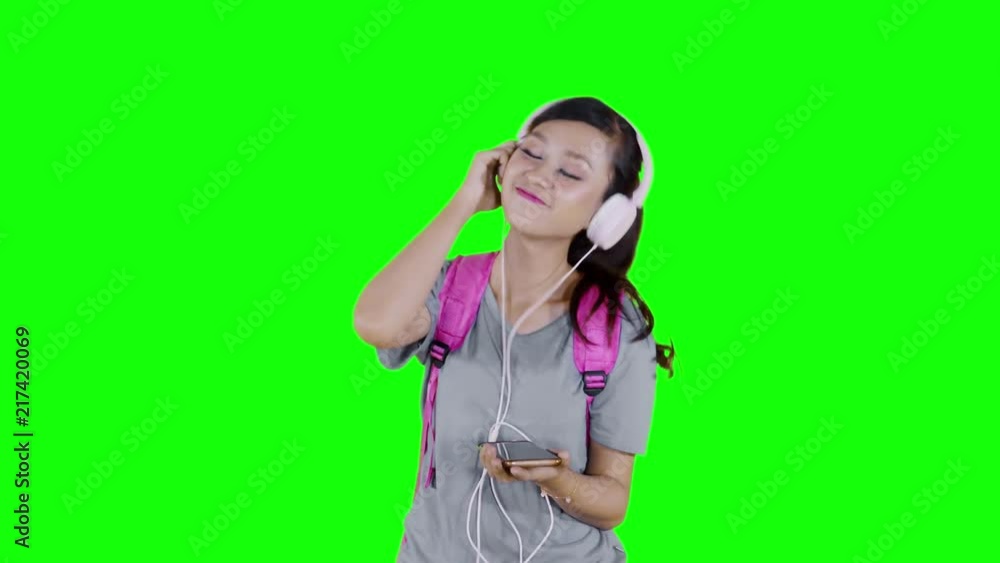 Beautiful female student enjoy music with mobile phone and headphone in the studio. Shot in 4k resolution with green screen background Beautiful female student enjoy music with mobile phone and headphone in the studio. Shot in 4k resolution with green screen background
