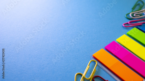 Multicolored paper clips and bookmarks on blue background. View from above with copy space