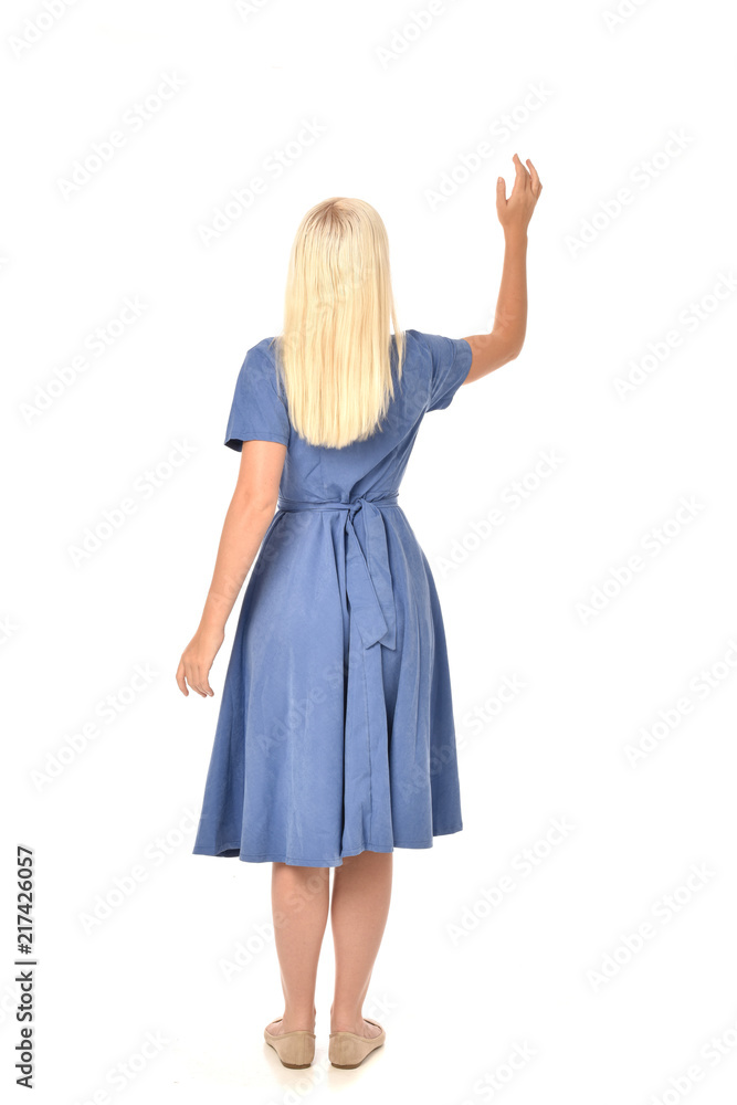 full length portrait of blonde girl wearing blue dress. standing pose with back to the camera. isolated on white studio background. full length portrait of blonde girl wearing blue dress. standing pose with back to the camera. isolated on white studio background.