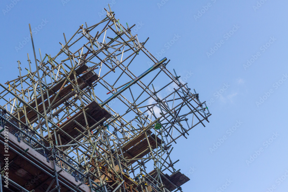 Construction scaffolding extending beyond the building into the blue sky. Seen from below