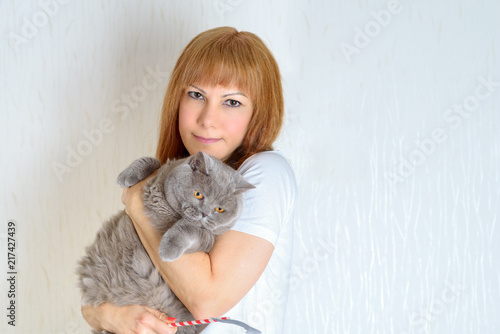 Attractive middle aged woman with cute british shorthair cat resting at home.A woman in the period of menopause. Blond / red hair mature senior female relaxing at home and embracing pet.