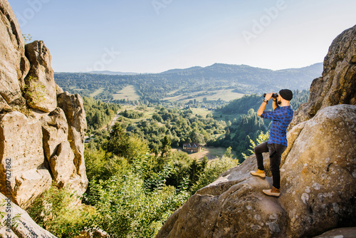 A man traveler standing on the top of mountain and lookin into the binoculars at the horizon