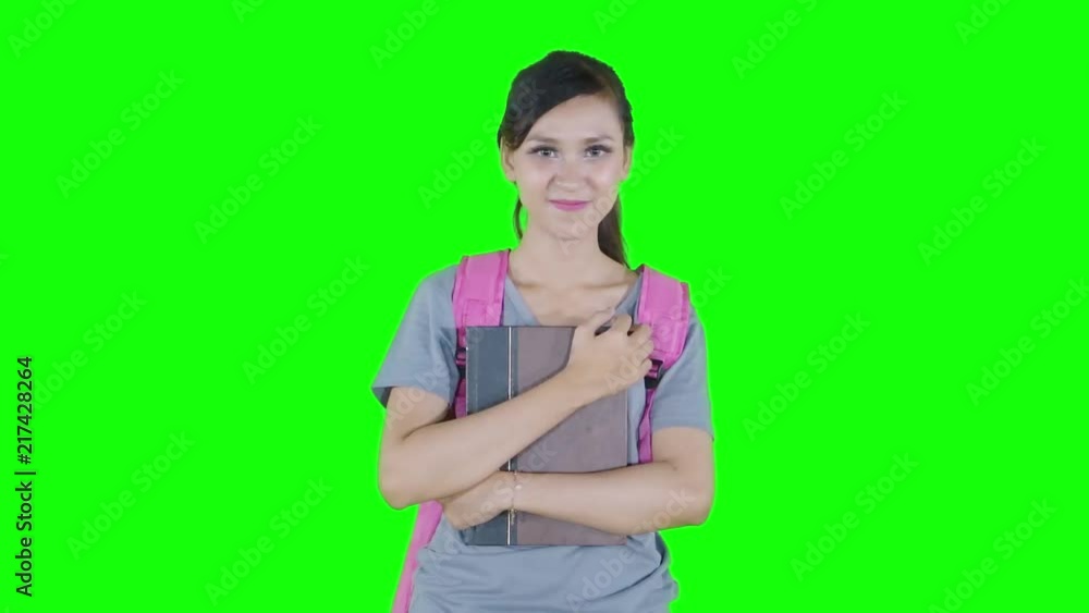 Beautiful female high school student showing thumb up while holding book in the studio. Shot in 4k resolution with green screen background Beautiful female high school student showing thumb up while holding book in the studio. Shot in 4k resolution with green screen background