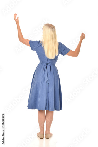full length portrait of blonde girl wearing blue dress. standing pose with back to the camera. isolated on white studio background.